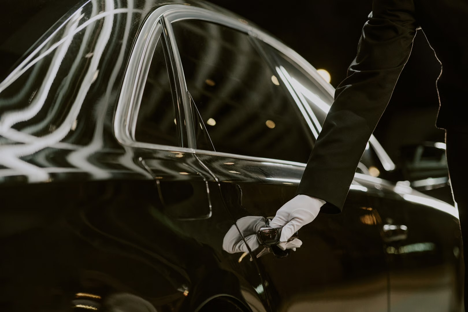 White-gloved chauffeur opening the door of a black luxury vehicle